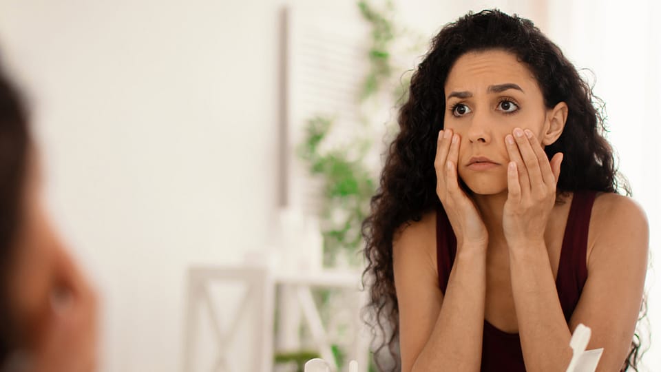 žena si v zrkadle prezerá kruhy pod očami